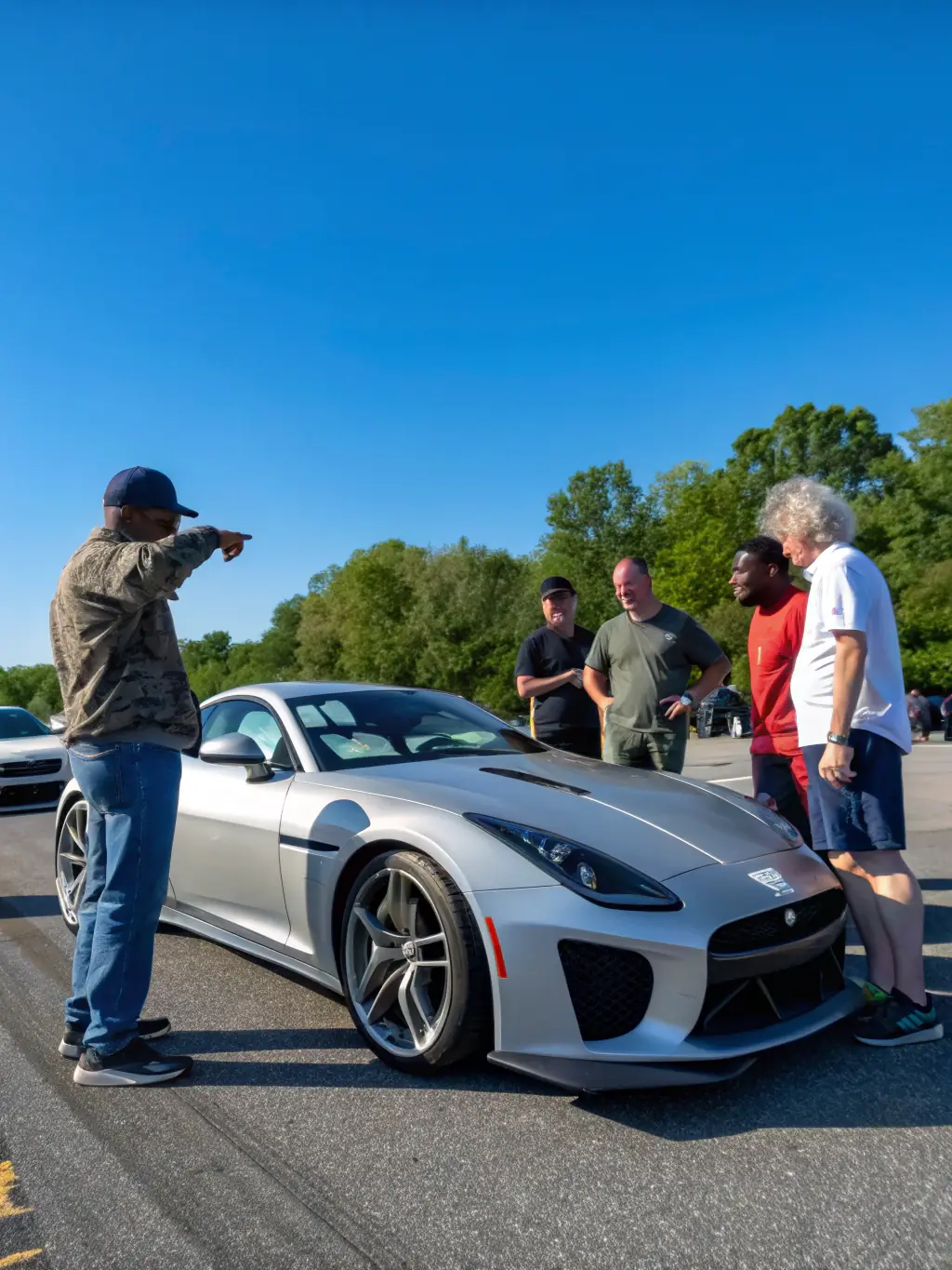 A group of Shifters club members gathered around a classic hot rod at a club event, smiling and engaged in conversation, showcasing the friendly and welcoming atmosphere of the club.